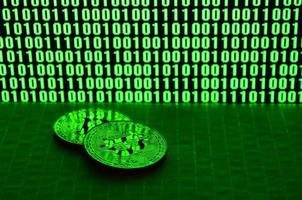 um par de bitcoins está em uma superfície de papelão no fundo de um monitor representando um código binário de zeros verdes brilhantes e unidades de um em um fundo preto. iluminação baixa chave foto