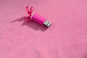cartão de memória flash usb rosa brilhante com um laço rosa encontra-se em um cobertor de tecido de lã rosa claro macio e peludo. design de presente feminino clássico para um cartão de memória foto