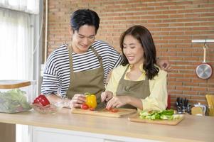 jovem casal asiático sorridente vestindo um avental na sala da cozinha, cozinhando o conceito foto