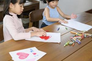 crianças asiáticas desenhando e pintando na mesa na sala de jogos em casa, jogo educativo. foto