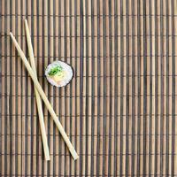rolo de sushi e pauzinhos de madeira estão em uma esteira de serragem de palha de bambu. comida asiática tradicional. vista do topo. minimalismo plano leigo com espaço de cópia foto