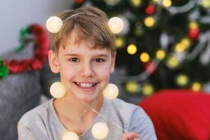 retrato de um menino feliz com luzes de natal na cabeça. foto