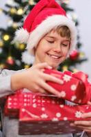 criança feliz no chapéu de papai noel segurando a pilha de presentes de natal foto