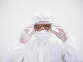 closeup de jovem médico asiático ou cientista em uniforme de conjunto de ppe segurando os óculos com as duas mãos enquanto olha para a frente. coronavírus ou covid-19 conceito isolado fundo branco foto