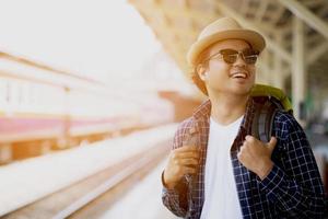 retrato o viajante turista jovem asiático com mochila e chapéu apreciando a vista feliz em sair na estação de trem com um viajante. conceito de viagem. foto