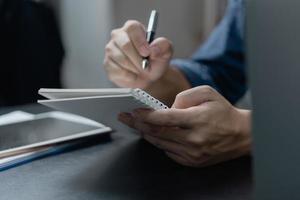 mão masculina escrevendo no caderno com caneta no computador portátil no escritório moderno. foto