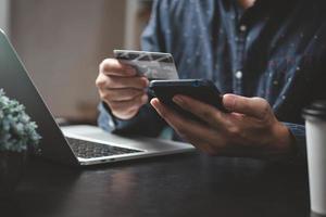 homem pagando e comprando com a tecnologia de aplicativo de carteira de comércio eletrônico de aplicativo para smartphone. homem usando telefone celular e cartão de crédito pagando via mobile banking. foto