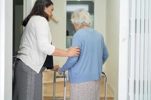 cuidador ajuda idosa asiática ou idosa a andar com suporte de andador subindo as escadas em casa. foto