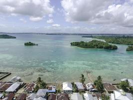 vista aérea da vila perto da bela praia com pequena ilha ao fundo em maluku, indonésia foto