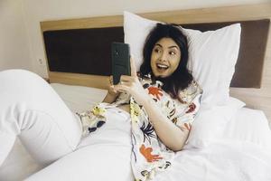 jovem feliz verificando em seu telefone enquanto estava deitada na cama foto