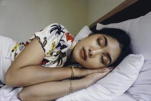 jovem mulher atraente dormindo no quarto, ela está deitada de lado e relaxando com os olhos fechados foto