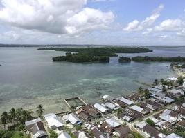 vista aérea da vila perto da bela praia com pequena ilha ao fundo em maluku, indonésia foto