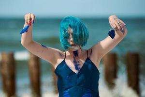 artista performática artística mulher de cabelos azuis manchada com tintas guache azul dançando na praia foto
