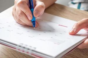 mão de mulher com caneta escrevendo na data do calendário conceito de reunião de planejamento de negócios foto