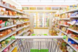 carrinho de compras com desfoque interior de prateleiras de corredor de loja de conveniência de supermercado para fundo foto