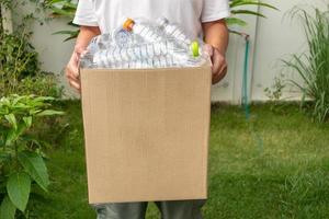 mão segurando a caixa de lixo reciclada marrom com garrafas plásticas foto