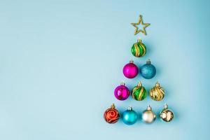 árvore de natal de enfeites e estrela dourada sobre fundo azul pastel