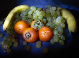 ainda vida de frutas. maçã, caqui e uvas em um fundo preto. camomila de caqui. gala de maçã. Alimentação saudável. gotas de água na fruta foto