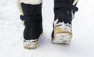 pés femininos em botas pretas andando na neve do inverno foto