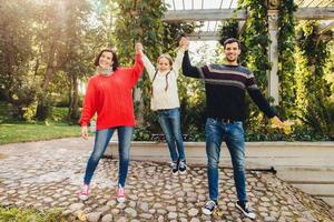 mulher bonita usa jeans e suéter vermelho, homem bonito mantém sua filha pequena com as mãos, tenta balançar ela, tem um tempo maravilhoso e inesquecível juntos ao ar livre. conceito de união. foto