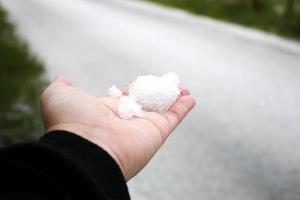 a mão de um homem segurando a neve na mão depois que neva contra uma estrada coberta de neve ao fundo. foto