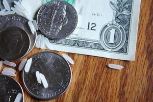 moedas de dólar e notas de dólar estão espalhadas em uma mesa de madeira com grãos de arroz. foto