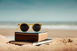 lendo livro ao ar livre no conceito de verão. livro e óculos de sol na areia da praia em frente ao mar em dia ensolarado. estilo de vida nas férias foto