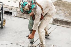 trabalhador da construção civil usando a superfície de concreto de perfuração de britadeira foto