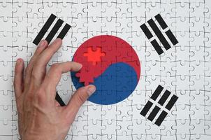 a bandeira da coreia do sul é retratada em um quebra-cabeça, que a mão do homem completa para dobrar foto