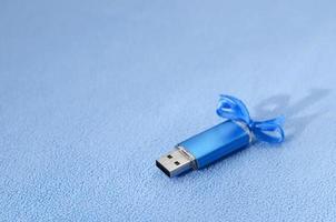 cartão de memória flash usb azul brilhante com um laço azul repousa sobre um cobertor de tecido de lã azul claro macio e peludo. design de presente feminino clássico para um cartão de memória foto