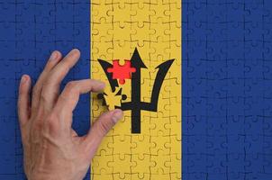 a bandeira de barbados é retratada em um quebra-cabeça, que a mão do homem completa para dobrar foto