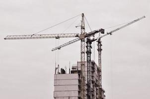 trabalhando guindastes altos dentro do lugar para edifícios altos em construção contra um céu azul claro. guindaste e construção de progresso de trabalho. tom retrô foto