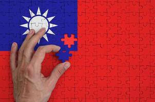 a bandeira de taiwan é retratada em um quebra-cabeça, que a mão do homem completa para dobrar foto