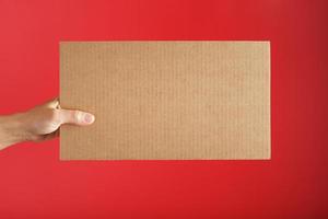 mão segurando uma folha de papelão em branco sobre um fundo vermelho. foto