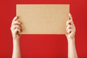 mãos segurando uma folha de papelão em branco sobre um fundo vermelho. foto