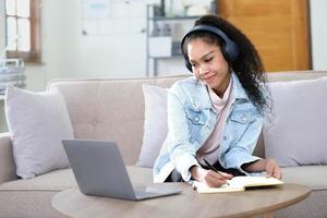 sorrindo jovem asiática usando fones de ouvido olhando para a tela do laptop ouvir e aprender cursos online. foto