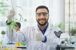 feliz homem do oriente médio cientista sorriso olhando mostrar folhas de cannabis pesquisa extrato químico alternativo de cannabis na fazenda agro laboratório, farmacêutico olhar microscópio erva folha ganja medicina alternativa foto