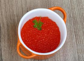 caviar vermelho em uma tigela sobre fundo de madeira foto