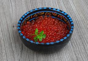 caviar vermelho em uma tigela sobre fundo de madeira foto