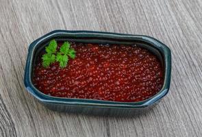 caviar vermelho em uma tigela sobre fundo de madeira foto