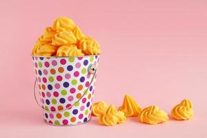 pequeno balde colorido cheio de merengue amarelo em um fundo rosa pastel. conceito mínimo com espaço de cópia. foto