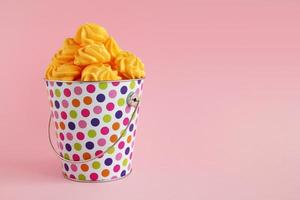 pequeno balde colorido cheio de merengue amarelo em um fundo rosa pastel. conceito mínimo com espaço de cópia. foto