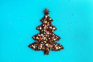 árvore de natal feita de grãos de café e estrela de anis decorada e polvilhação culinária multicolorida sobre um fundo azul, vista superior. foto