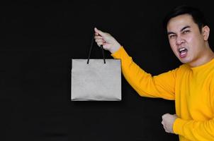 macho feliz asiático segurando sacolas de compras em fundo escuro para o conceito de sexta-feira negra. foto