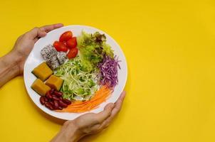 mãos segurando um prato de salada vegana em fundo amarelo para o festival de nove deuses do imperador ou festival vegetariano na tailândia que celebra por 9 dias na véspera do 9º mês lunar do calendário chinês. foto