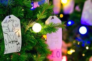 papel pendurado na árvore de natal para decoração de férias com luzes coloridas no fundo. foto