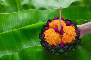 mão segurando folha de bananeira krathong que tem 3 incensos e vela decora com flores para a lua cheia da tailândia ou festival loy krathong. foto