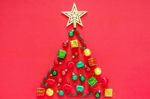 árvore de natal feita de decorações de ornamento de ano novo em fundo vermelho. conceito de férias mínimas planas leigas. foto