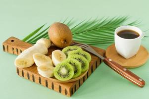 café da manhã com xícara de café e frutas. fatias frescas de kiwi e banana. conceito de café da manhã saudável foto