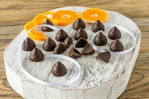 balas de geléia de laranja cobertas com chocolate amargo e saboroso. saborosos doces na placa de madeira branca foto